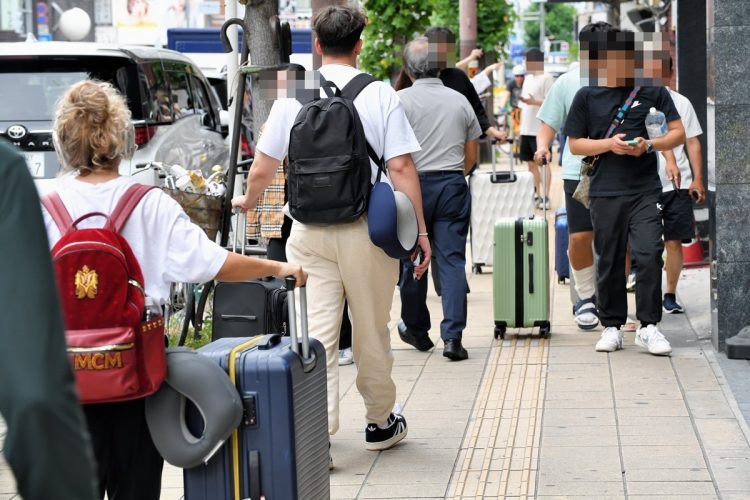 日本橋周辺で大きなスーツケースを引きながら歩く外国人観光客